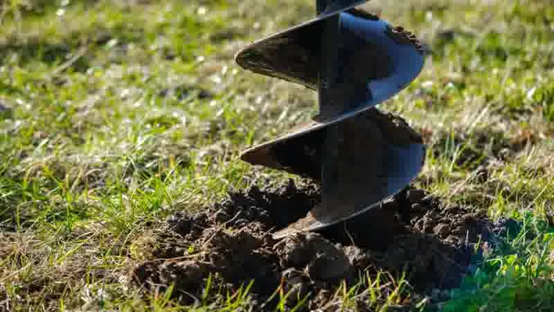 Contractor using a power auger to dig a fence post hole